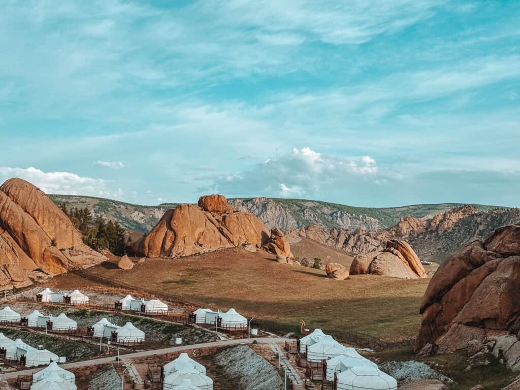 Yurt camp set against rocky red cliffs and grassy plains in Terelj Mongolia